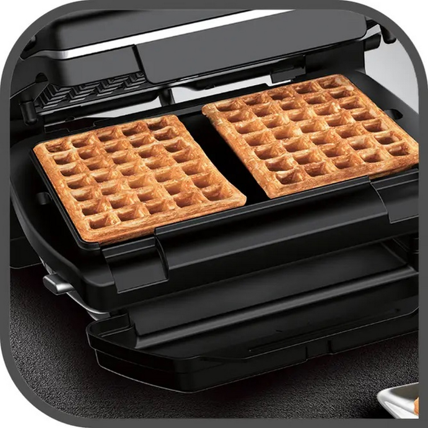 Two golden-brown waffles are in a black waffle maker. The maker is open, waffles ready to eat.