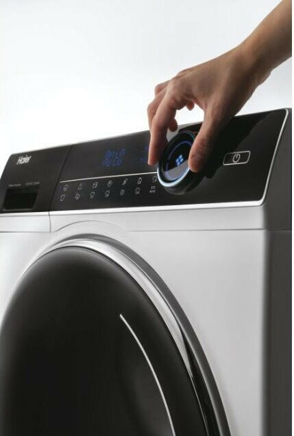 Dłoń obracająca pokrętło na panelu sterowania pralki Haier.
