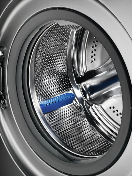 Zbliżenie bębna pralki z niebieskim plastikowym elementem w środku, odbijającym otoczenie.
