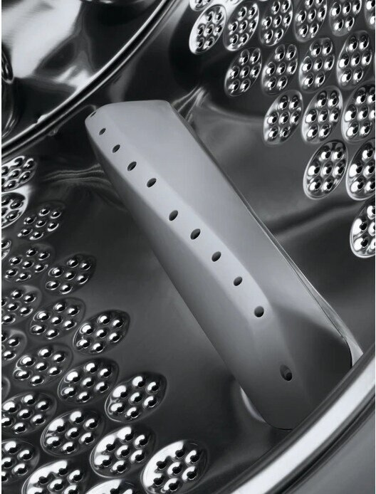 Zbliżenie wnętrza bębna pralki. Perforowana stal nierdzewna z białym plastikowym mieszadłem.