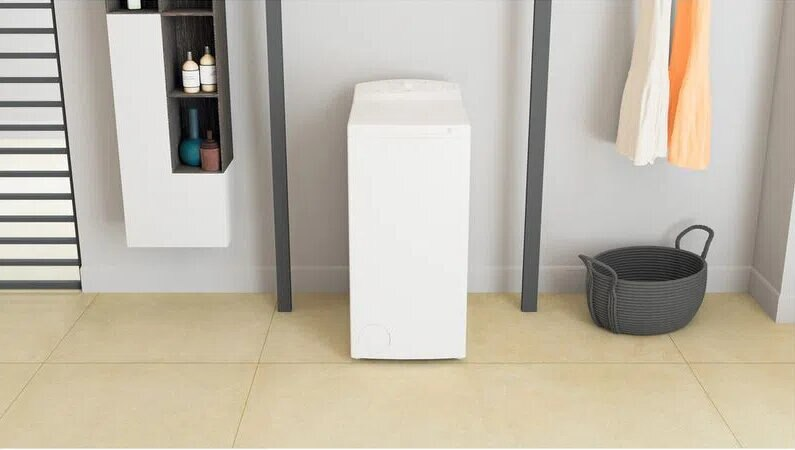 Biała pralka w pokoju. Kosz i ubrania po prawej.