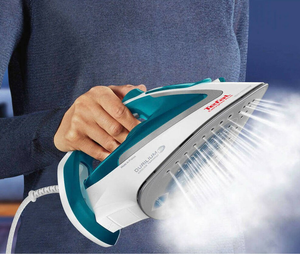 Osoba trzymająca niebiesko-białe żelazko, wydobywa się para.