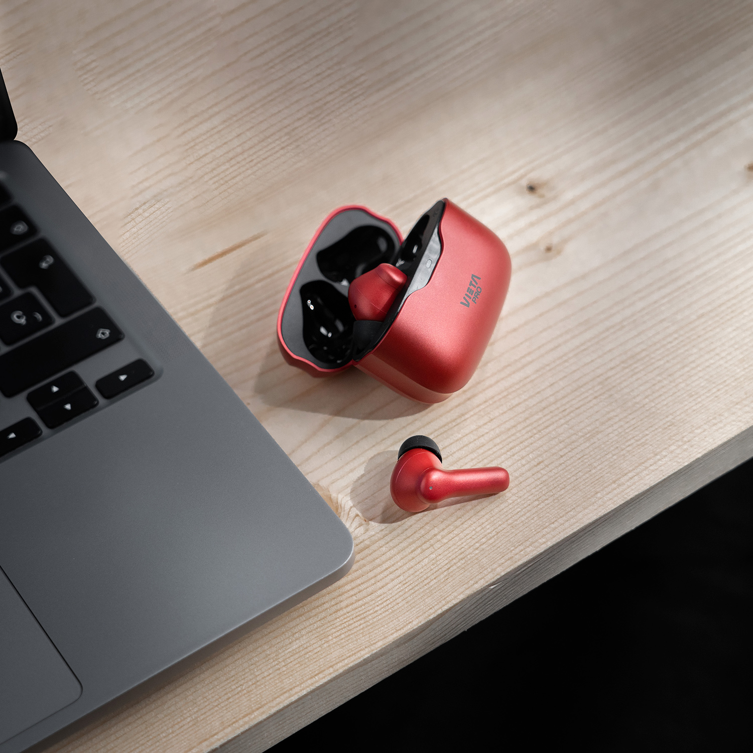Auriculares rojos en un estuche rojo sobre una superficie de madera, cerca de una laptop.
