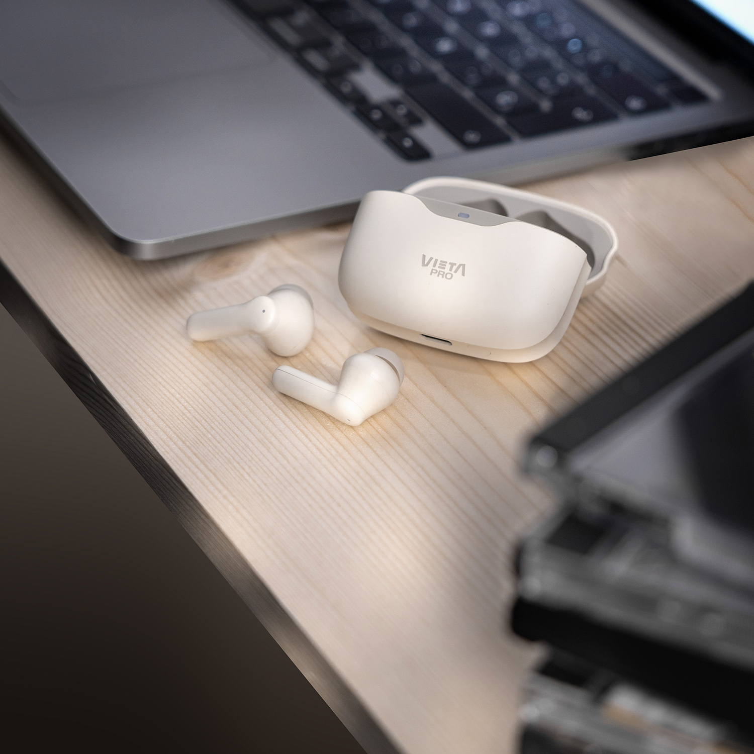 Auriculares blancos, estuche de carga y portátil sobre mesa de madera, con CDs.