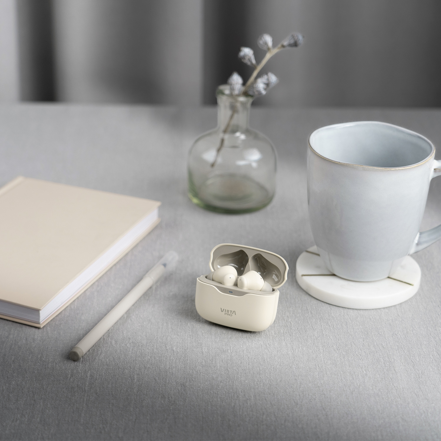 Naturaleza muerta con auriculares, un cuaderno, un bolígrafo, un jarrón pequeño y una taza sobre una mesa.