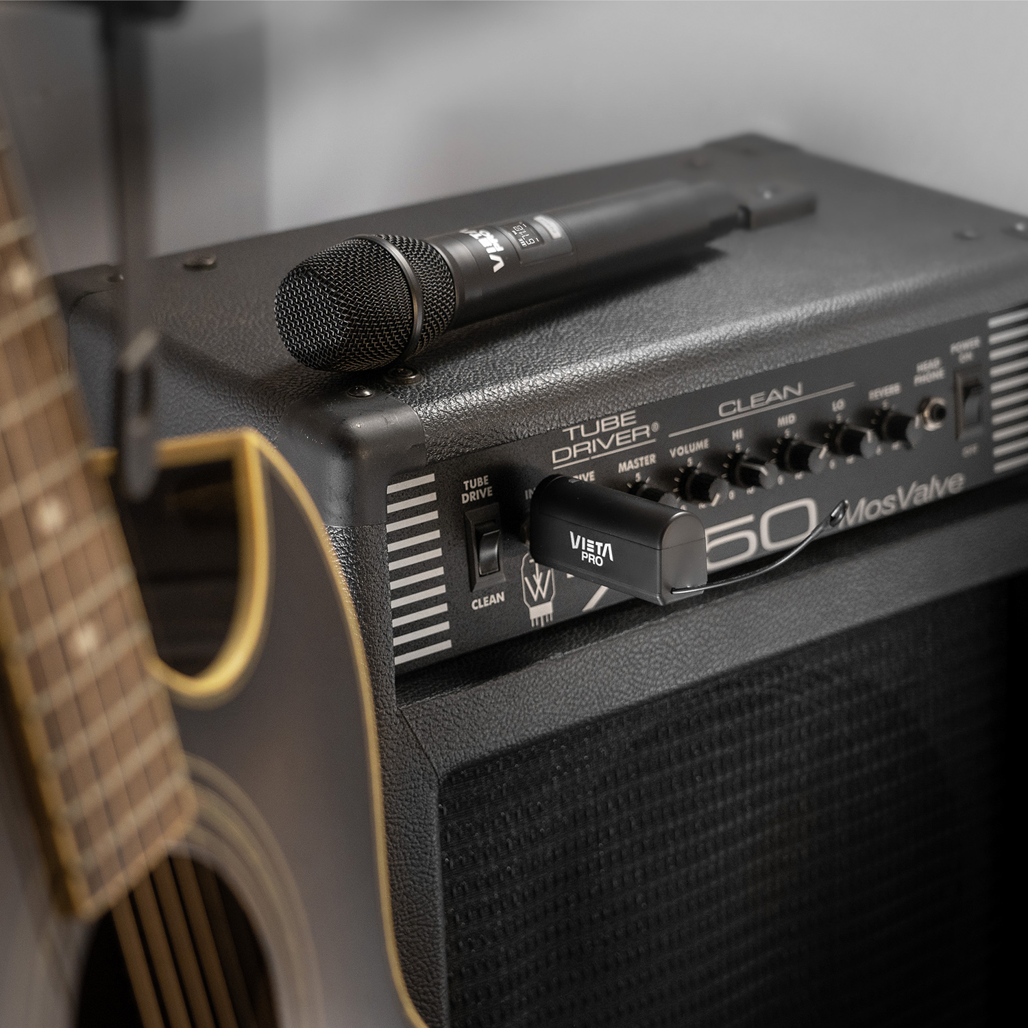 Micrófono y receptor sobre amplificador negro, con guitarra en primer plano.