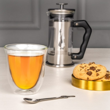 Tea egy pohárban, francia prés. Süti egy arany tányéron, kanál az asztalon.