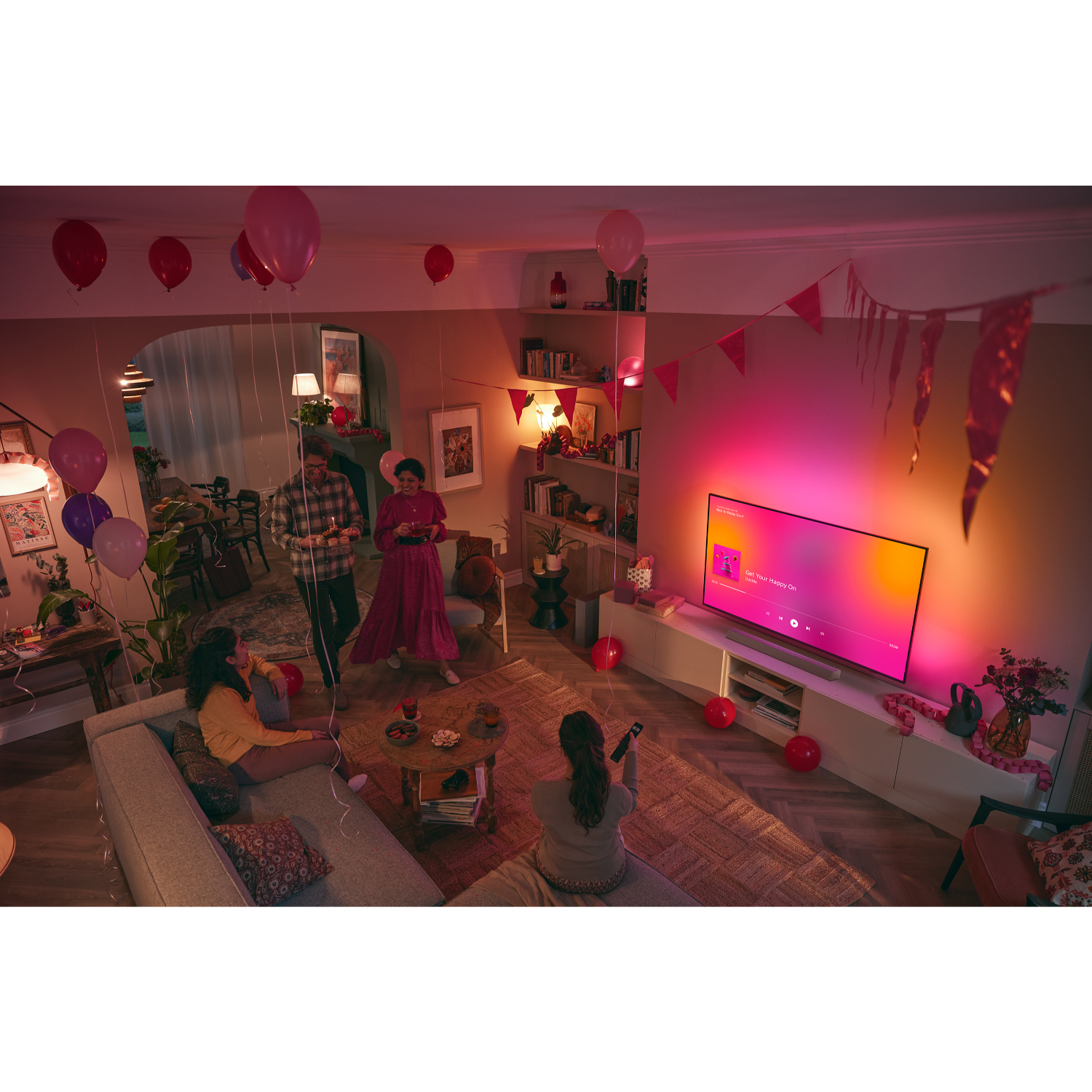 Mensen in een woonkamer met tv, ballonnen en decoraties. Er zijn mensen aan het socializen.