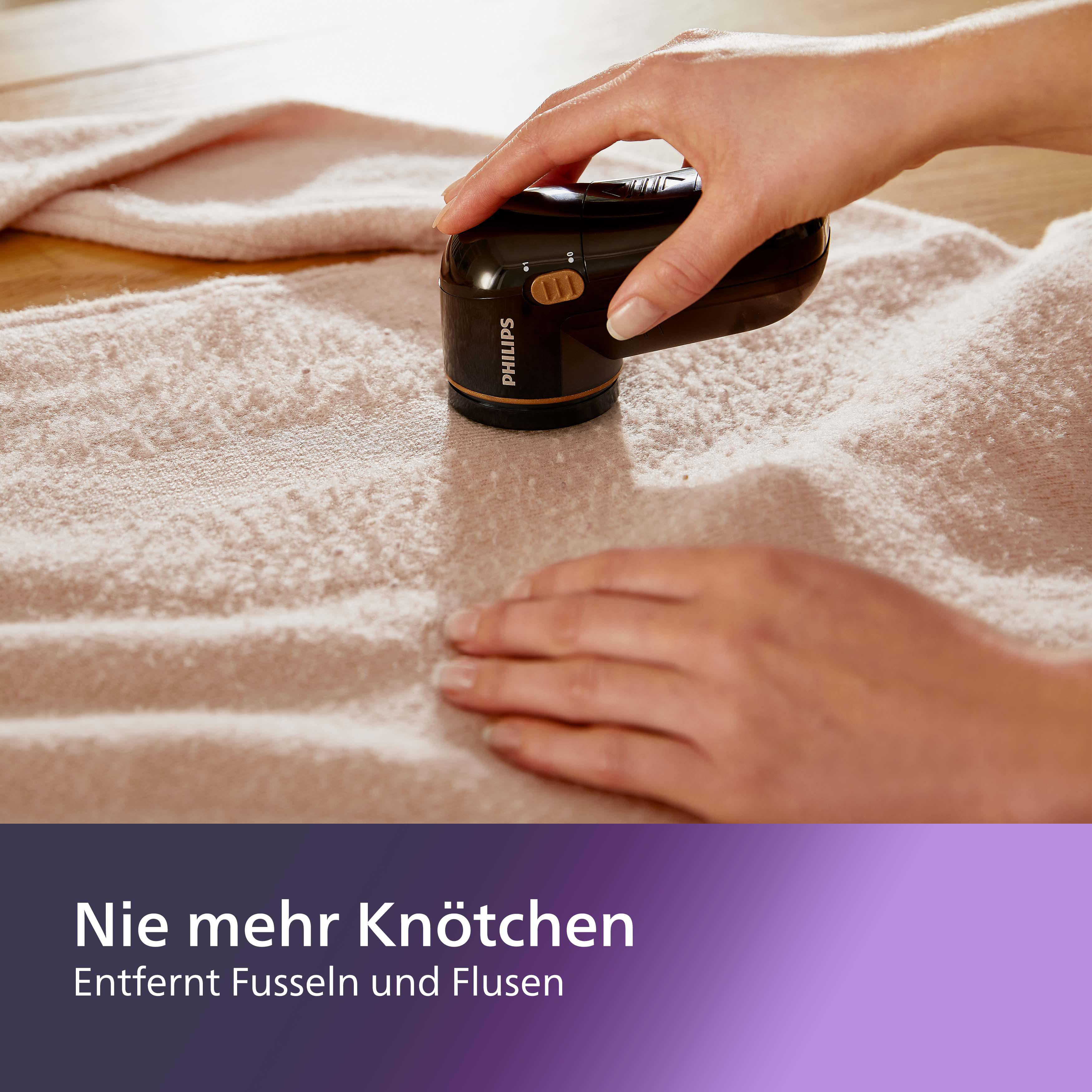 Ein Philips Stoffrasierer wird auf einem rosa Pullover verwendet, um Fusseln zu entfernen.