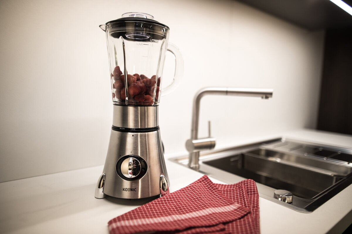 Blender z truskawkami w środku, stojący na białym blacie.