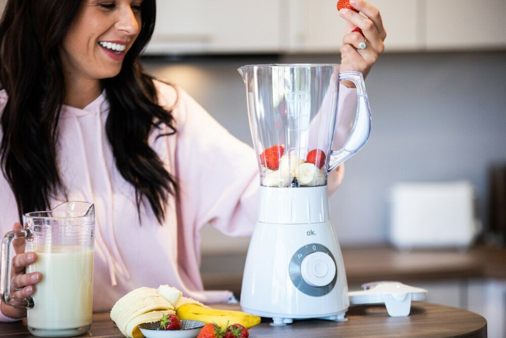 Kobieta wrzuca truskawkę do białego blendera z owocami.