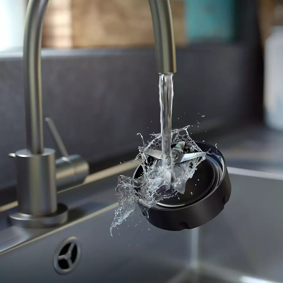 Woda pryska z kubka blendera z ostrzami nad zlewem.
