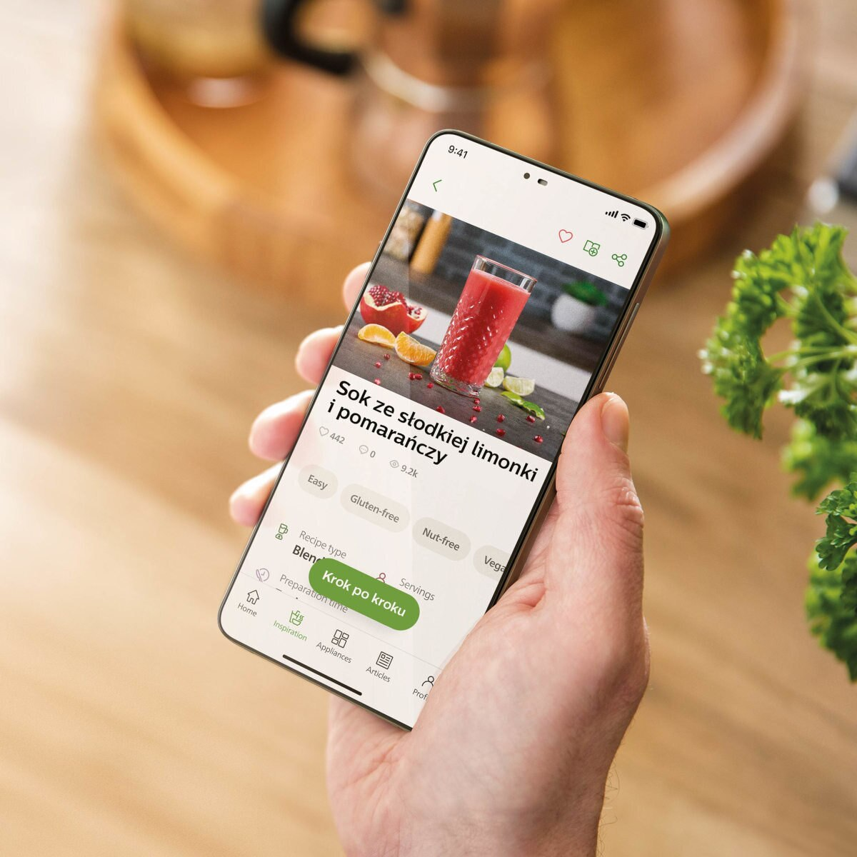 Ręka trzymająca telefon z przepisem. Koktajl na ekranie. Drewniane tło.