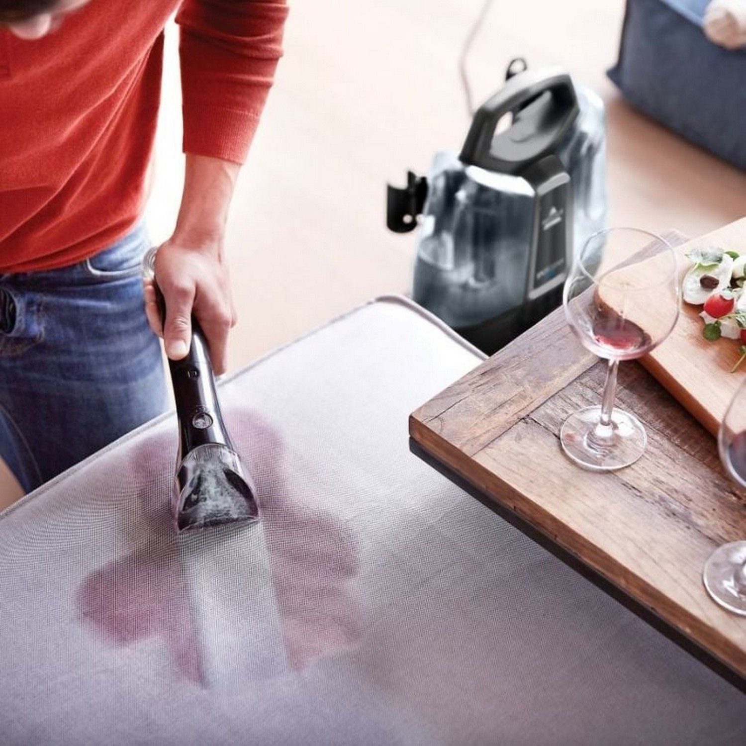 Personne nettoyant un canapé avec une machine, tache rouge.