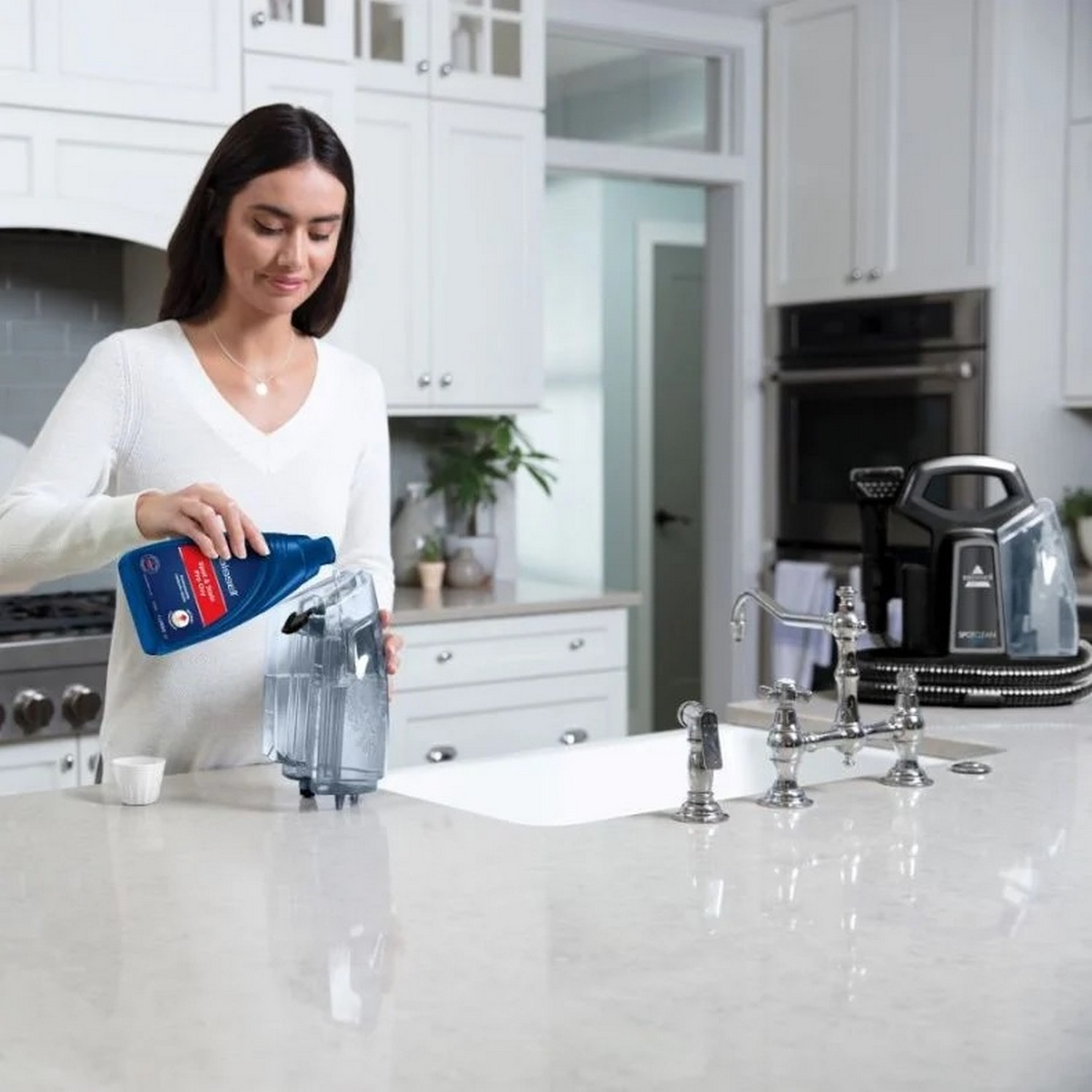 Une femme verse une solution de nettoyage bleue dans un récipient. Cadre de cuisine blanc avec évier et comptoir.