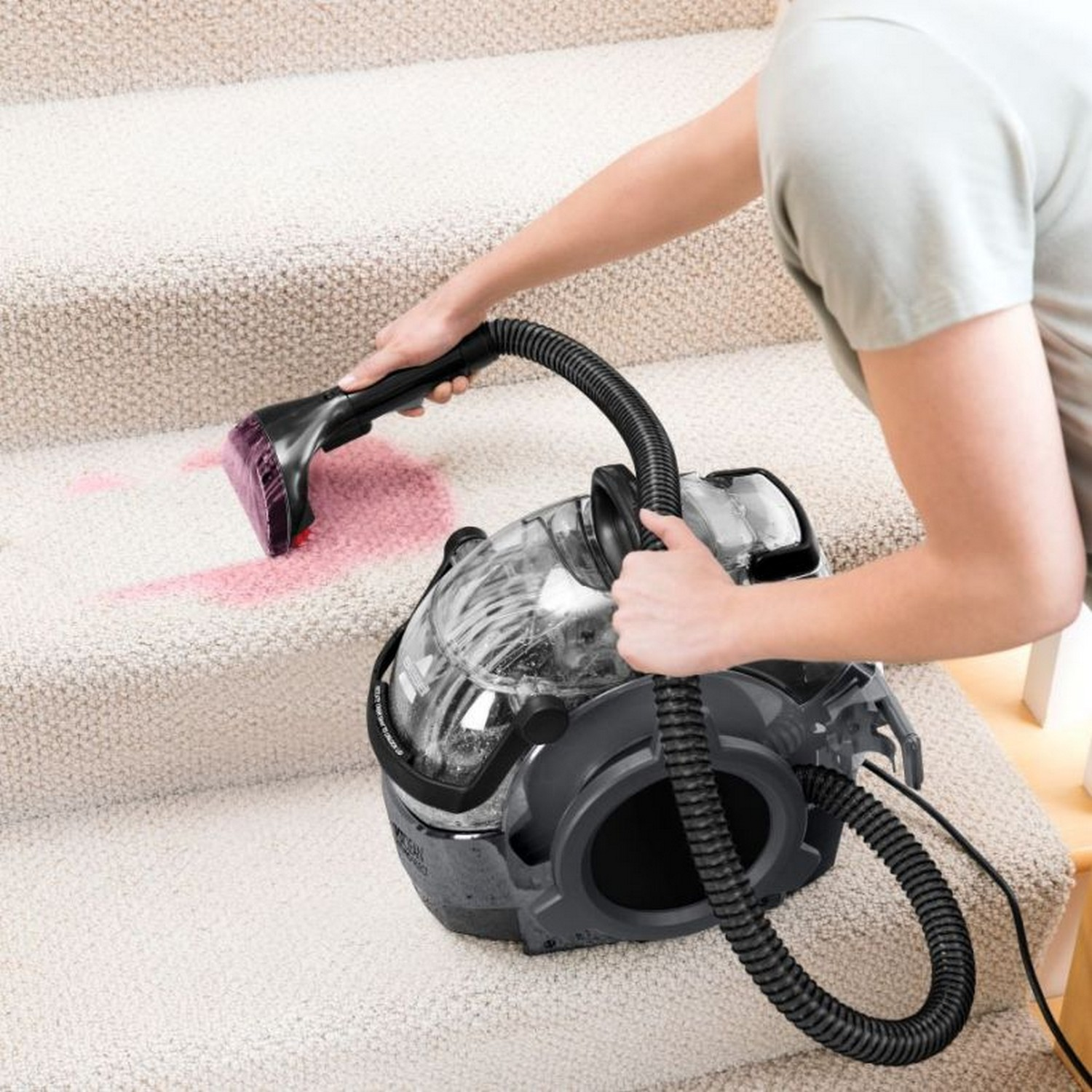 Une personne utilise un nettoyeur de tapis sur un escalier, enlevant une tache rouge.