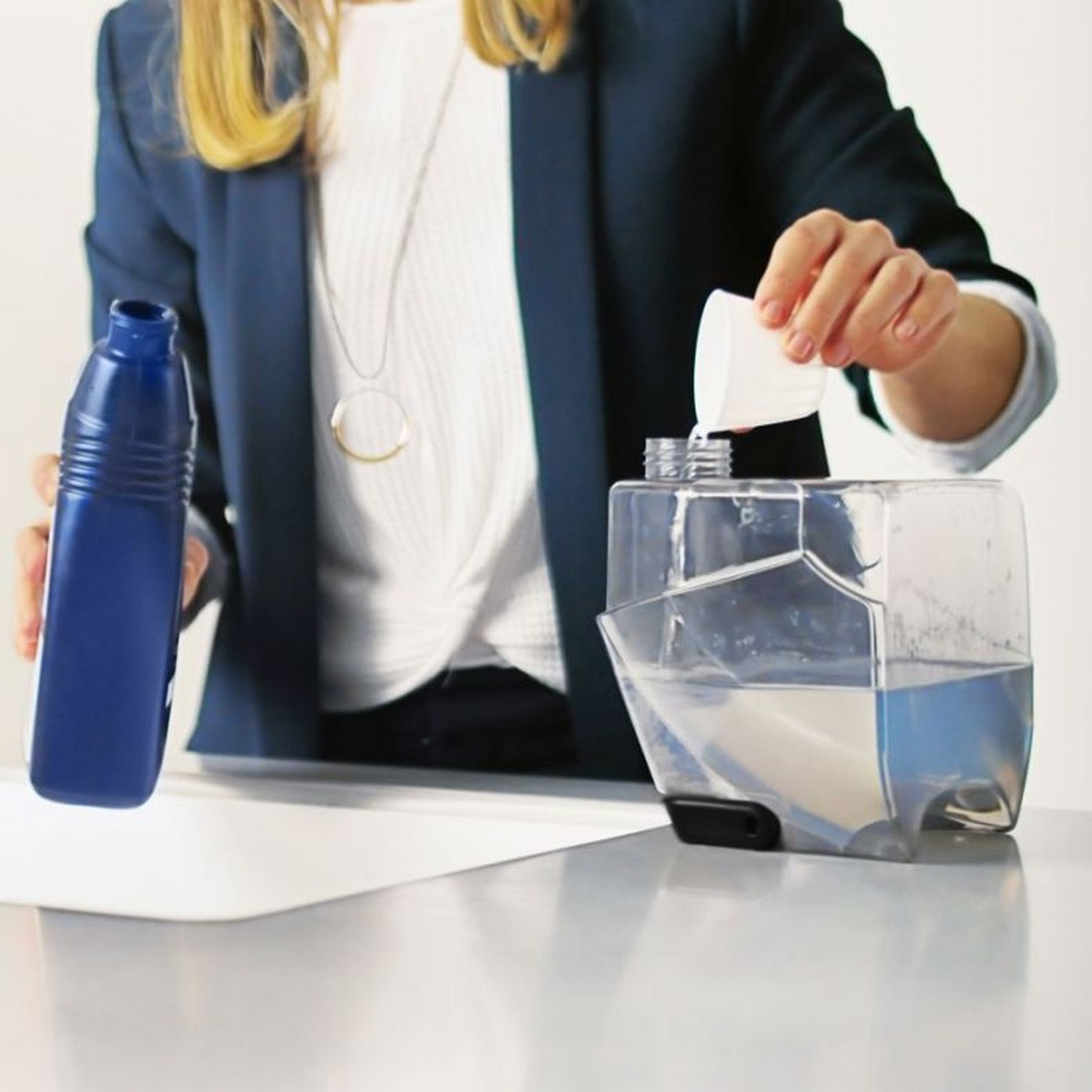 Personne versant du produit de nettoyage dans un appareil. Bouteille bleue à côté.