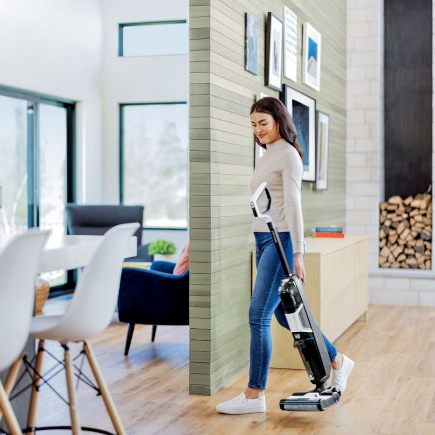 Femme passant l'aspirateur sur un sol en bois dans un salon moderne avec des meubles blancs.