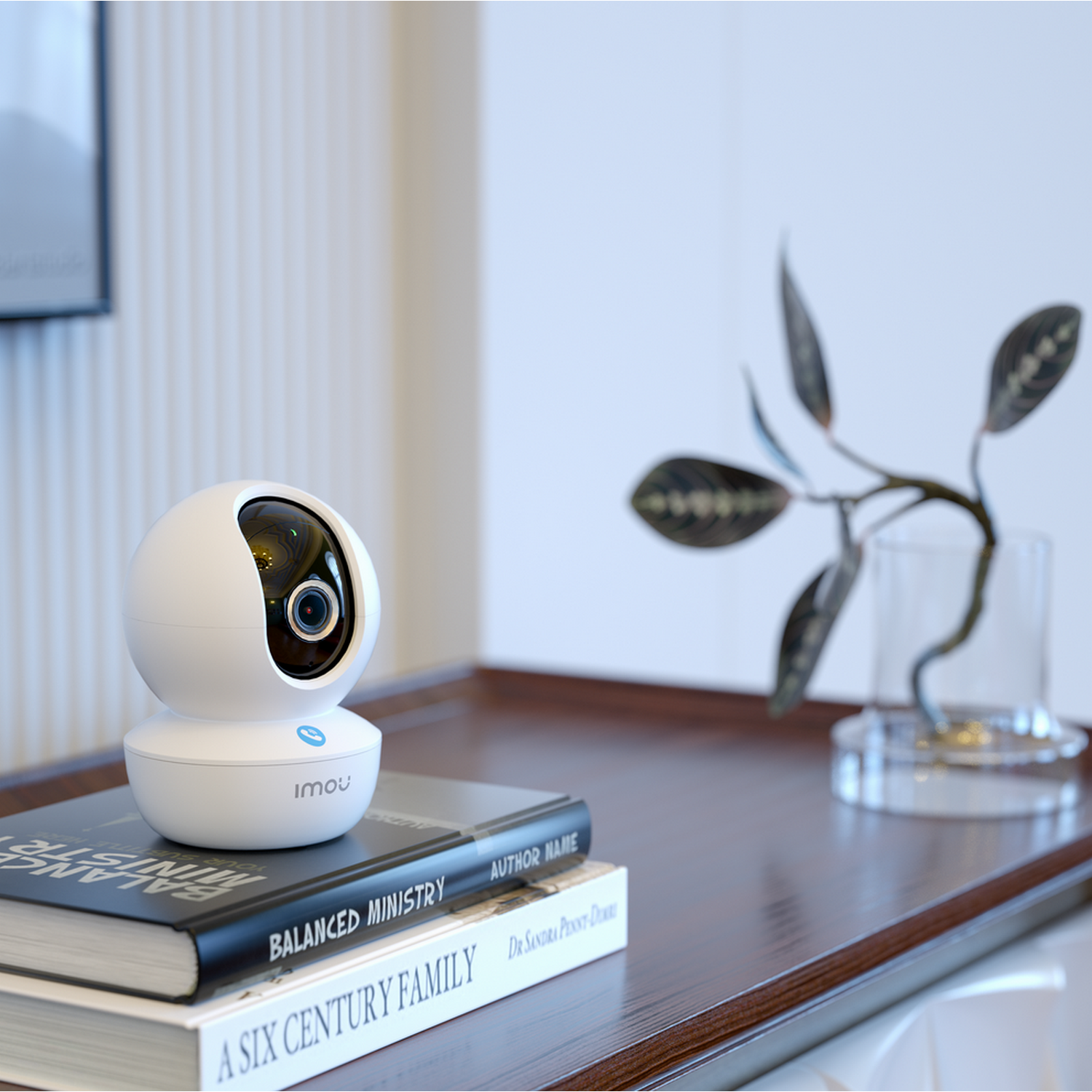 White security camera on a table with books and a plant. Background is blurred.