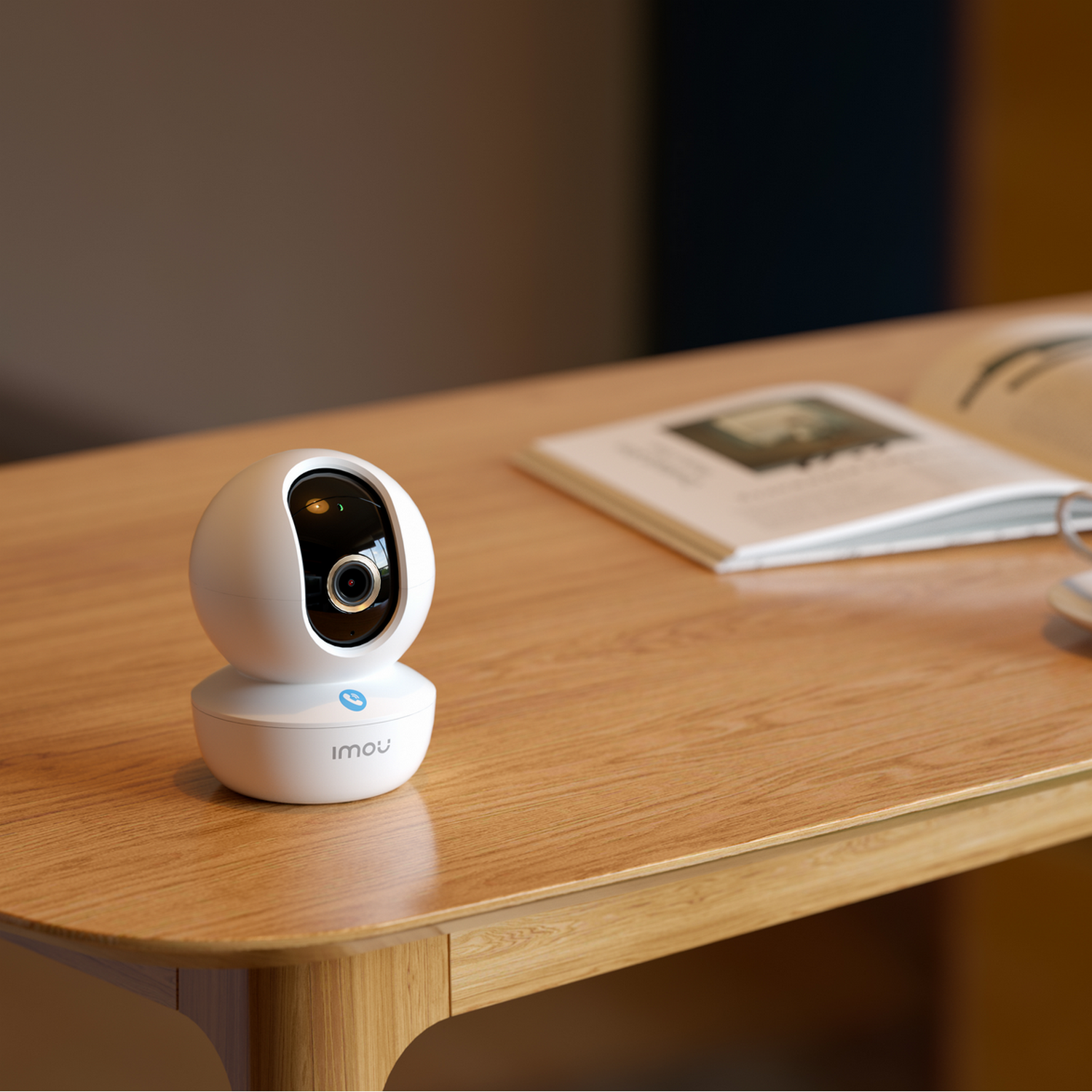 White security camera on a wooden table. A book and a pen are near it.