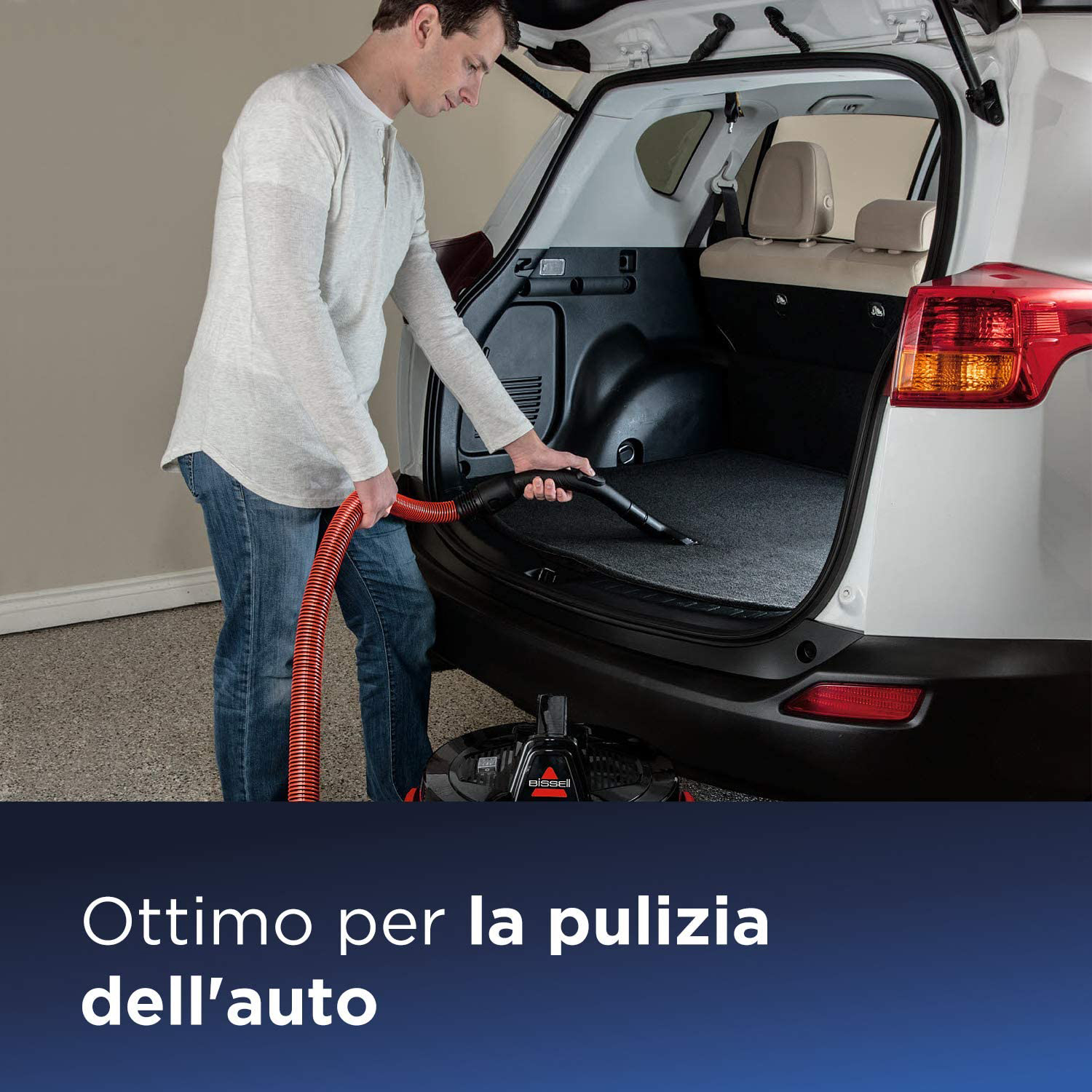 Un uomo che aspira l'interno di un'auto, usando un tubo rosso.