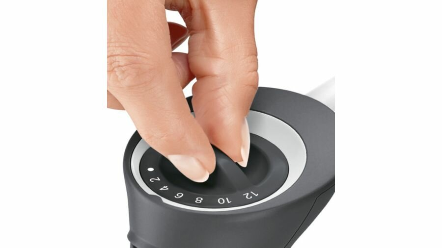 Zbliżenie dłoni obracającej pokrętło na szarym urządzeniu.