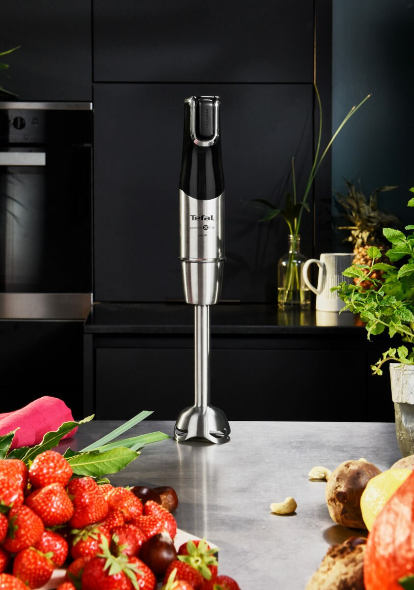 Stalowy blender ręczny na blacie kuchennym z truskawkami i innymi przedmiotami.