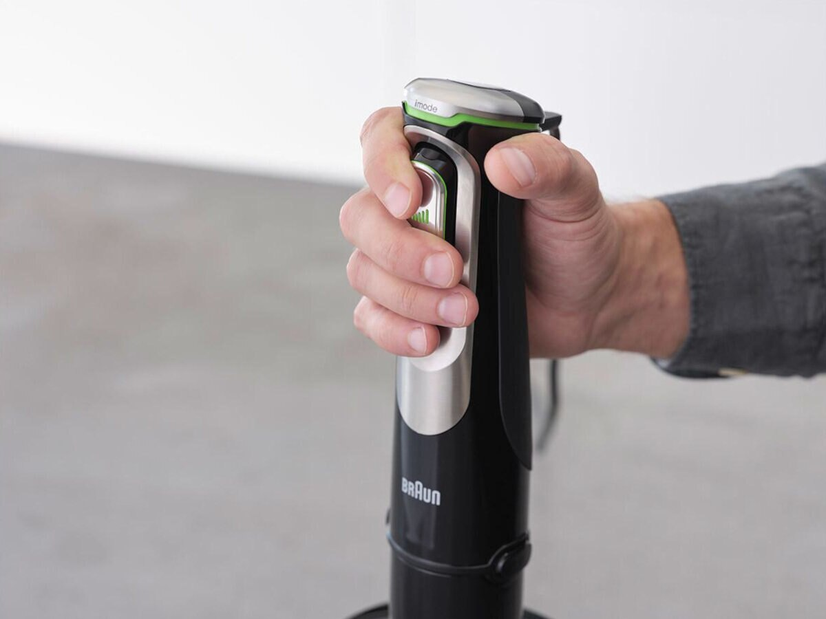 Ręka trzyma czarno-srebrny blender ręczny Braun.