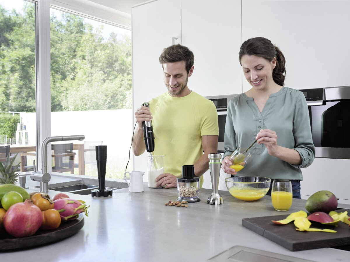 Dwie osoby w kuchni, jedna używa blendera ręcznego, druga ubija jajka.