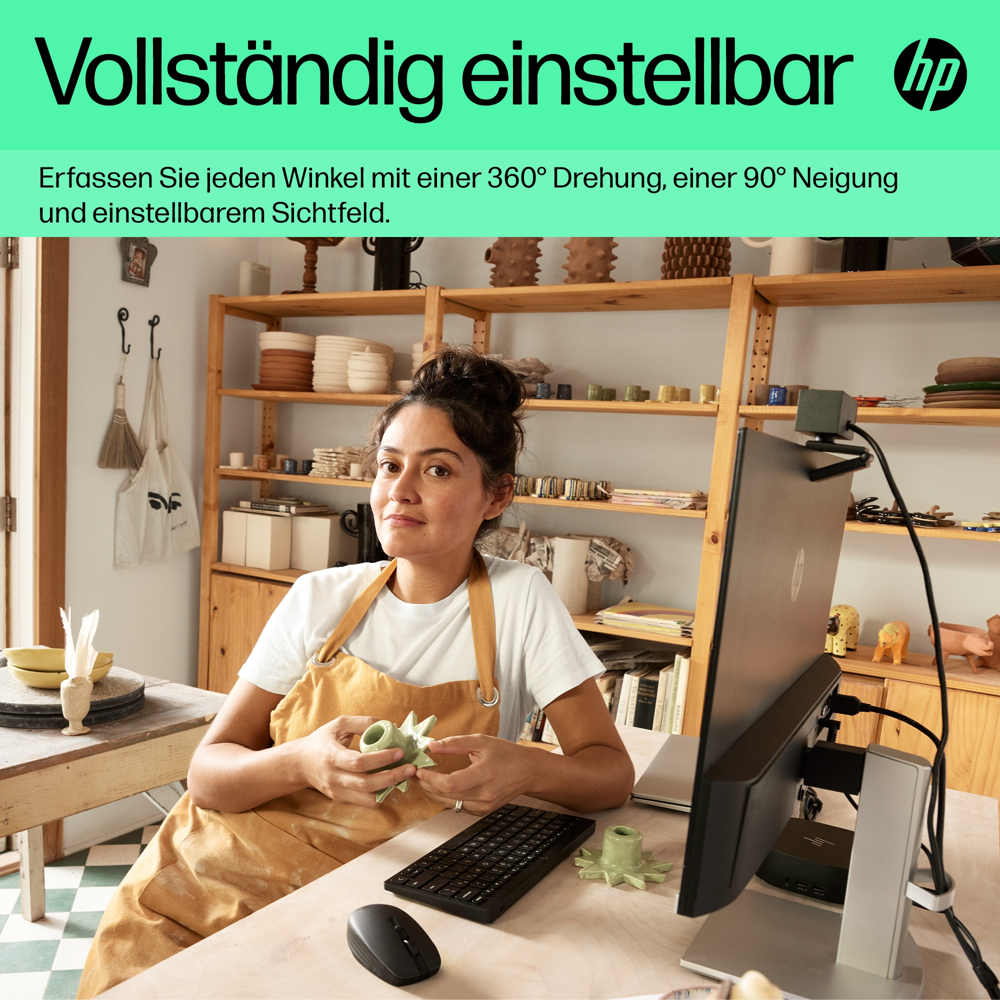 Frau mit Schürze und Computer, hält grünen Gegenstand, in Werkstatteinstellung.