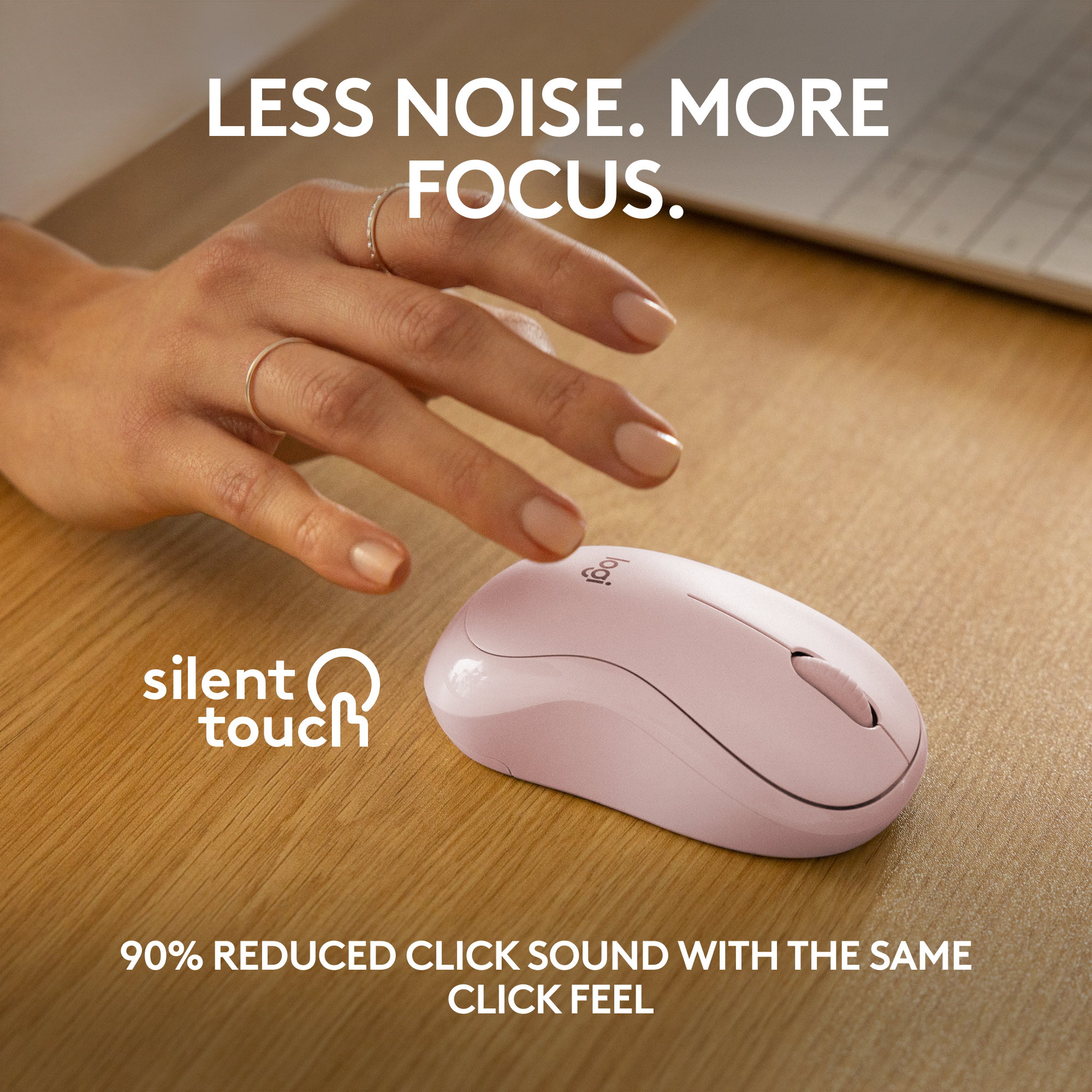 Une souris sans fil rose sur un bureau en bois. Une main pointe vers la souris.