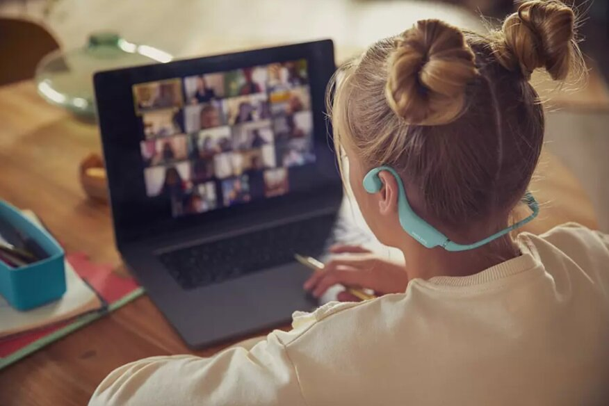 Młoda dziewczyna z kokami w słuchawkach uczestniczy w rozmowie wideo na laptopie.