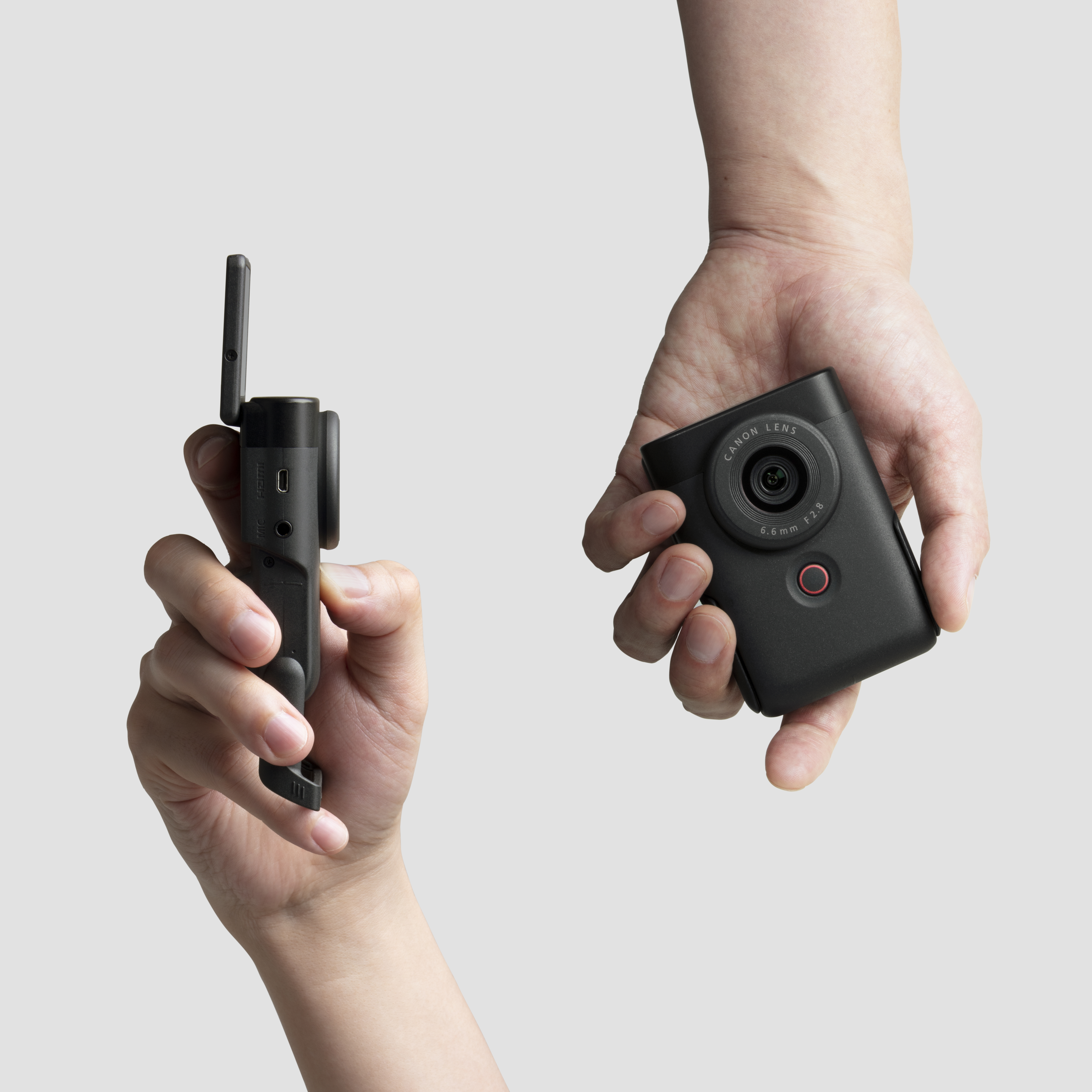 Two hands holding a black camera with a lens, and a black accessory with a handle.