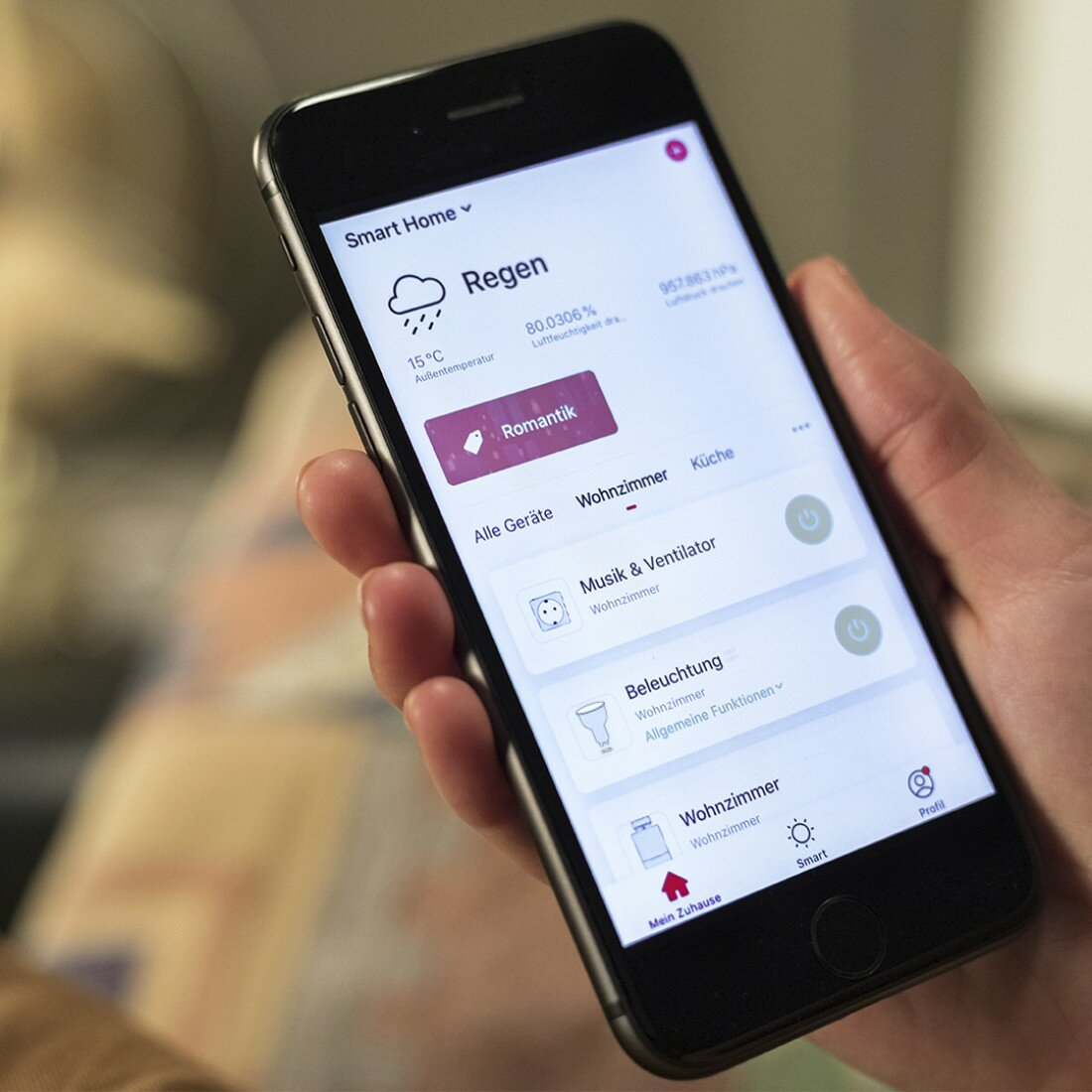 Dłoń trzymająca smartfon z interfejsem smart home, pokazującym pogodę i kontrolki.