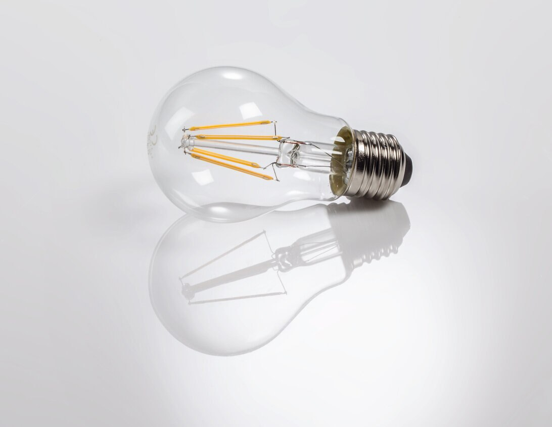 Przezroczysta żarówka na odblaskowej powierzchni, z widocznymi wewnętrznymi włóknami.