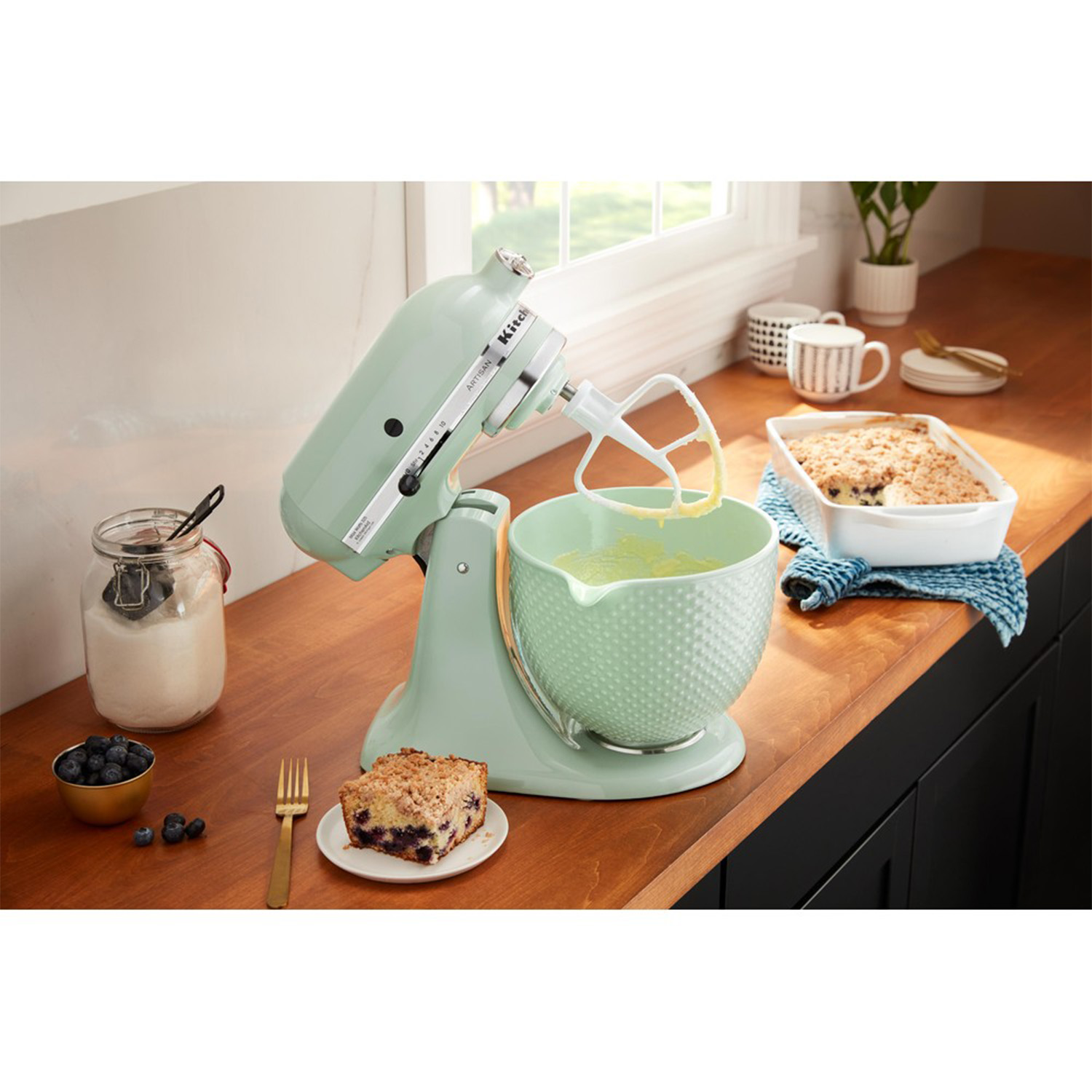 Un mixer KitchenAid verde menta che mescola l'impasto in una ciotola, con altri elementi di cottura.