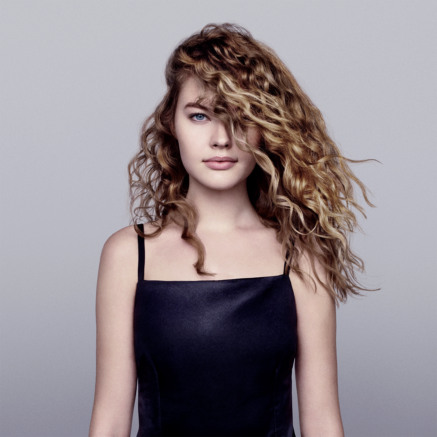 Una giovane donna con capelli biondi ondulati, indossa un top nero, guarda avanti.
