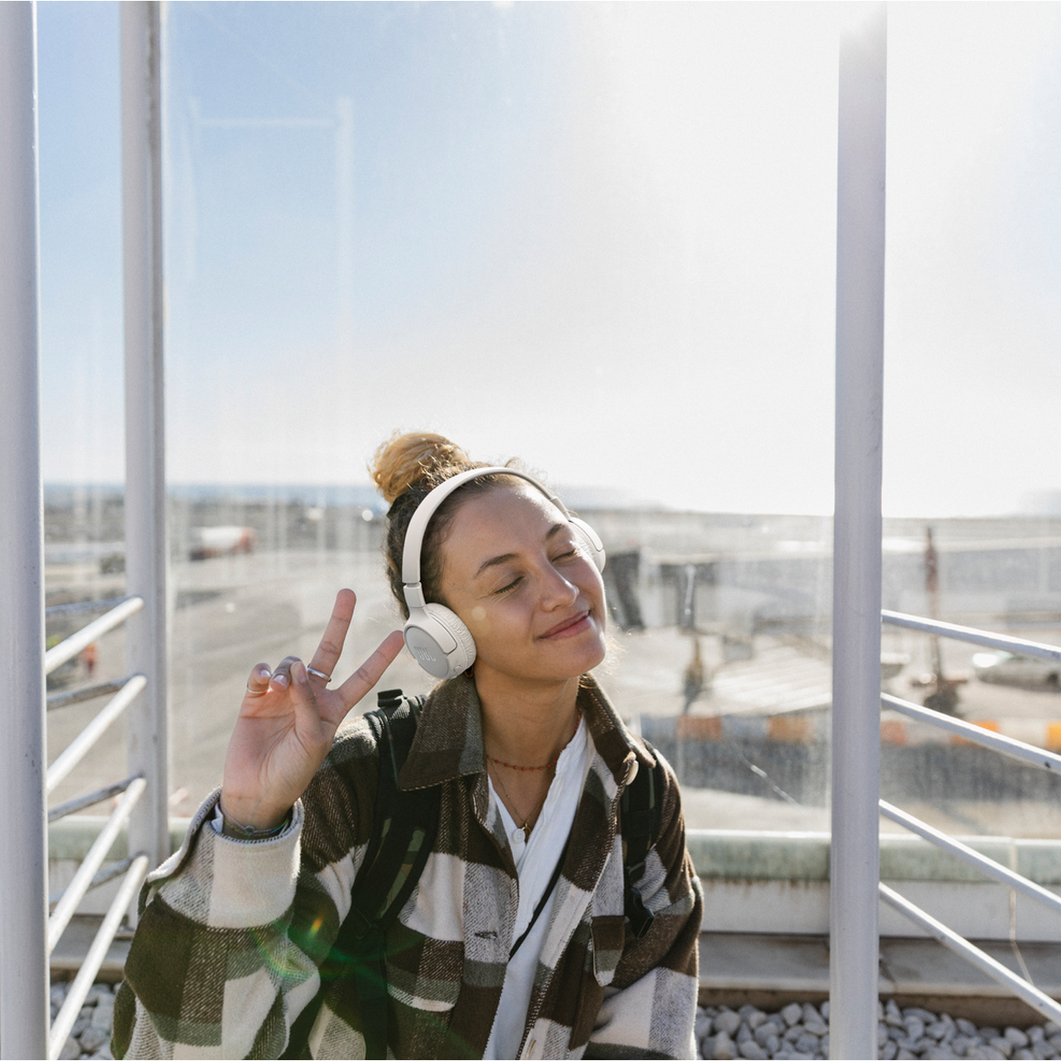 Woman wearing headphones, making a peace sign, standing in front of a glass wall.