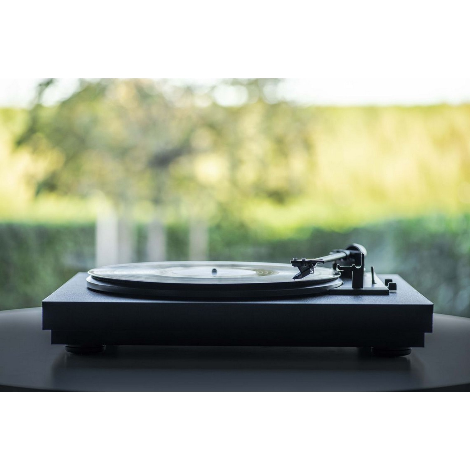 Platine vinyle noire sur une table, avec un disque en rotation et une fenêtre en arrière-plan.