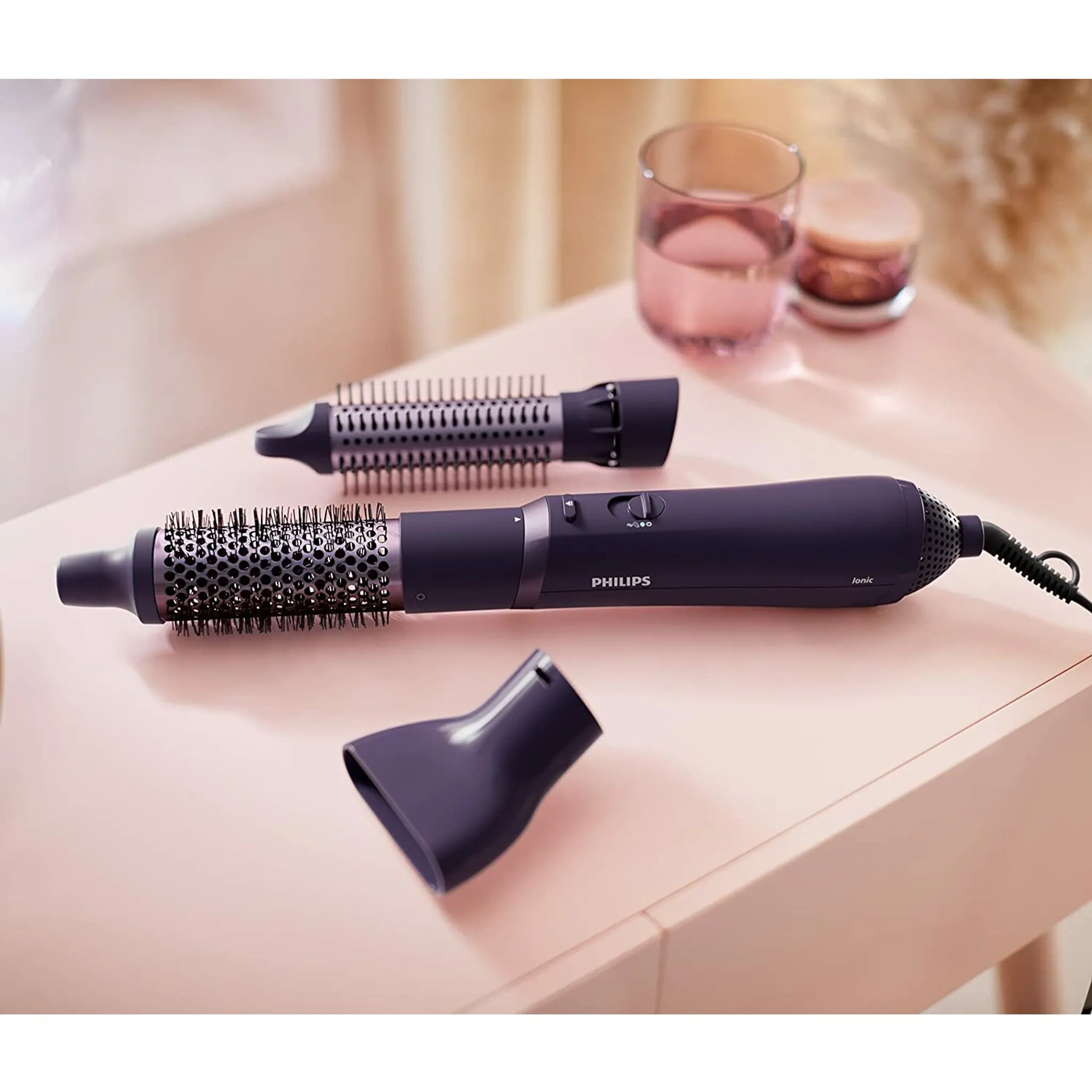 Juego de moldeador de cabello Philips púrpura y accesorios sobre una superficie rosa.