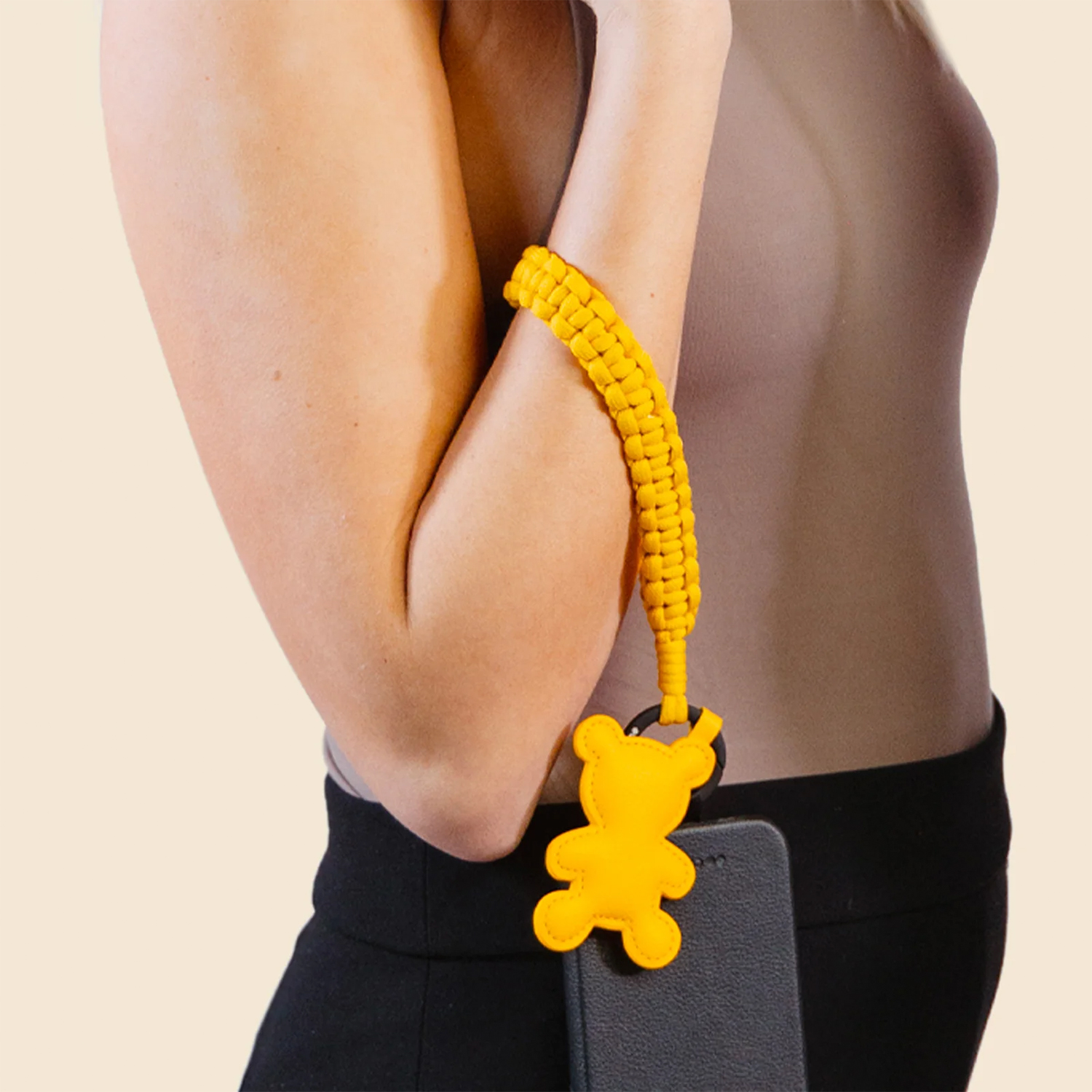 Una persona che indossa un cinturino da polso per telefono giallo intrecciato con un ciondolo a forma di orso giallo.