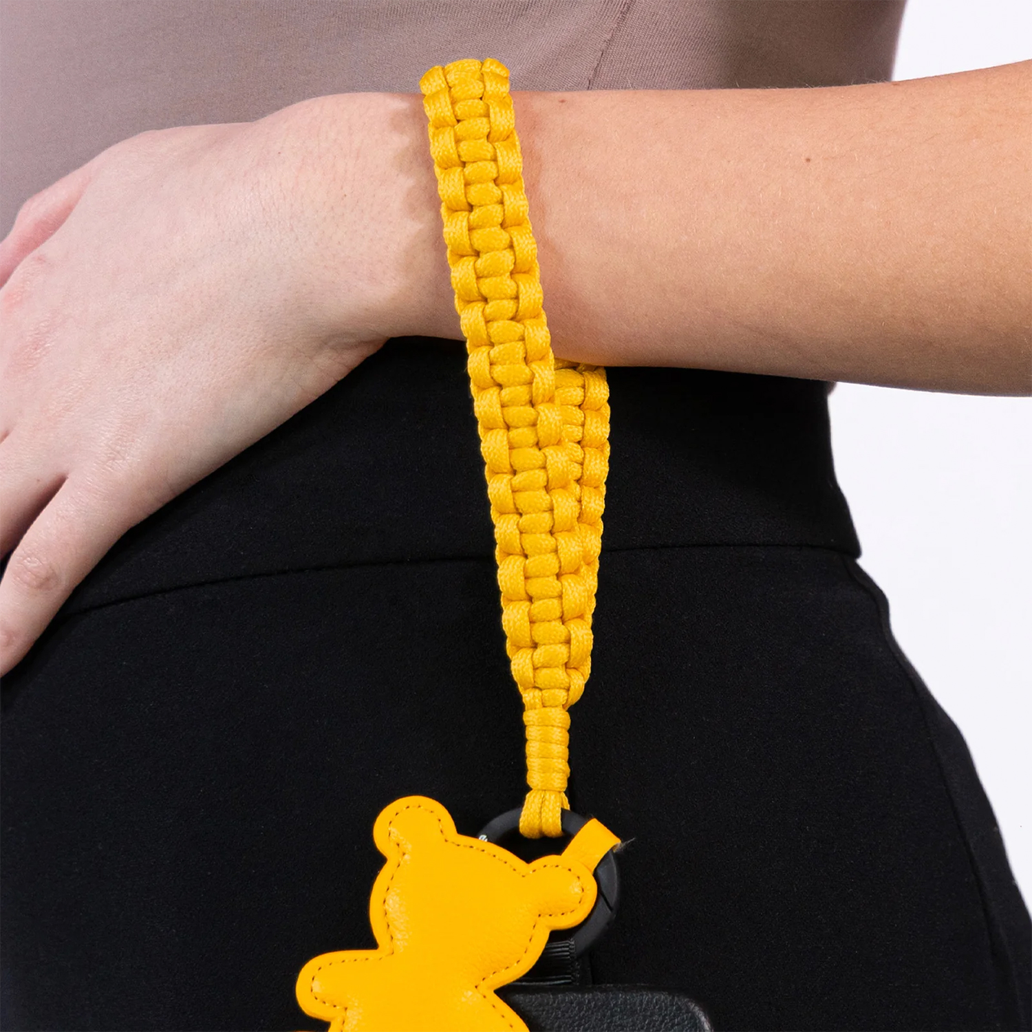 Il polso di una persona con un cinturino in corda giallo e un ciondolo a forma di orsetto giallo.