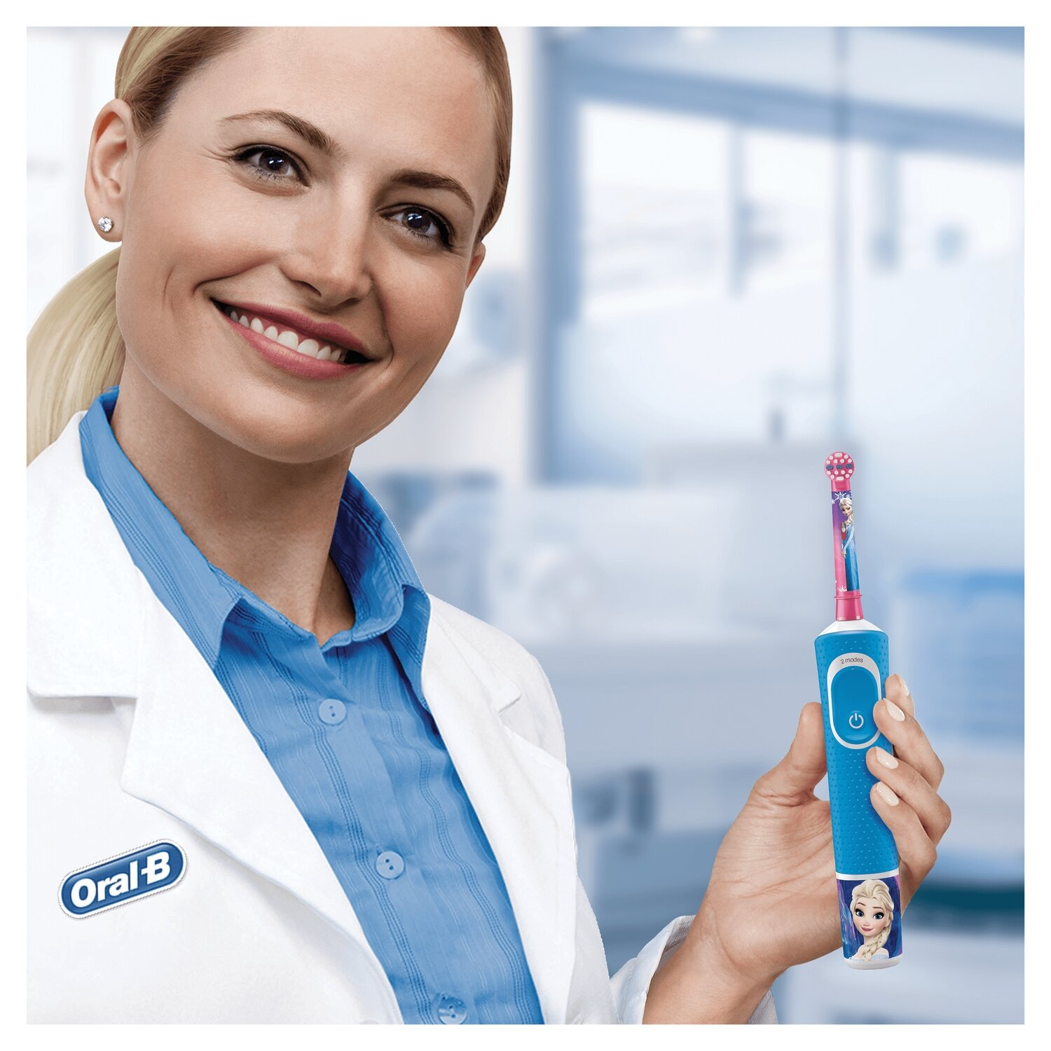 Kobieta w kitlu trzyma niebieską szczoteczkę Oral-B z Elsą z Krainy Lodu. Uśmiechnięta.