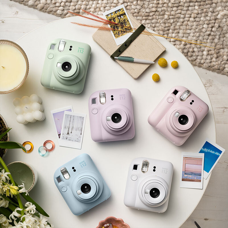 Pięć aparatów Instax Mini 11 w różnych pastelowych kolorach na białym stole z akcesoriami.