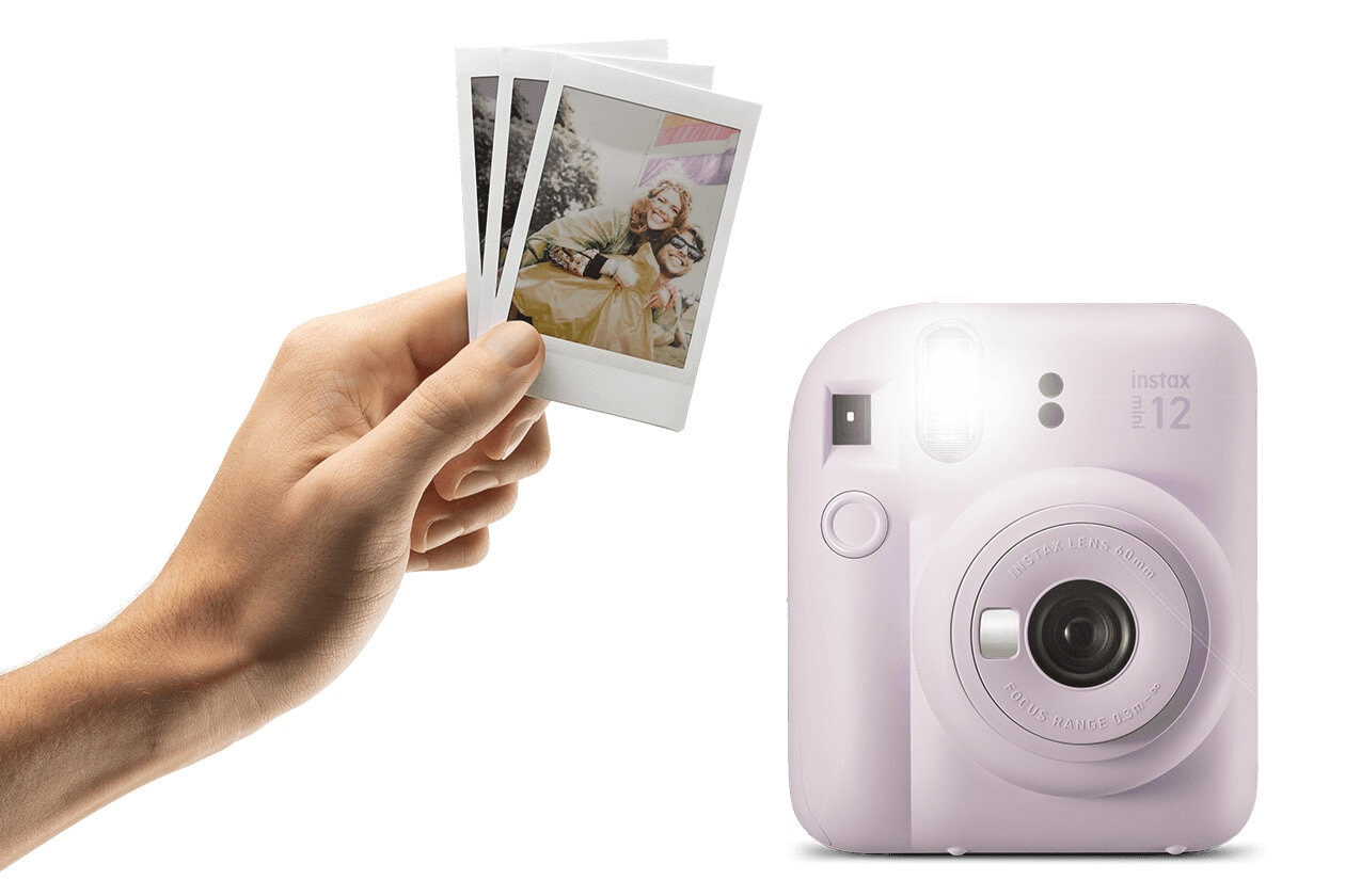 Różowy aparat Instax z trzema wydrukowanymi zdjęciami. Ręka trzyma odbitki, lampa błyskowa włączona.