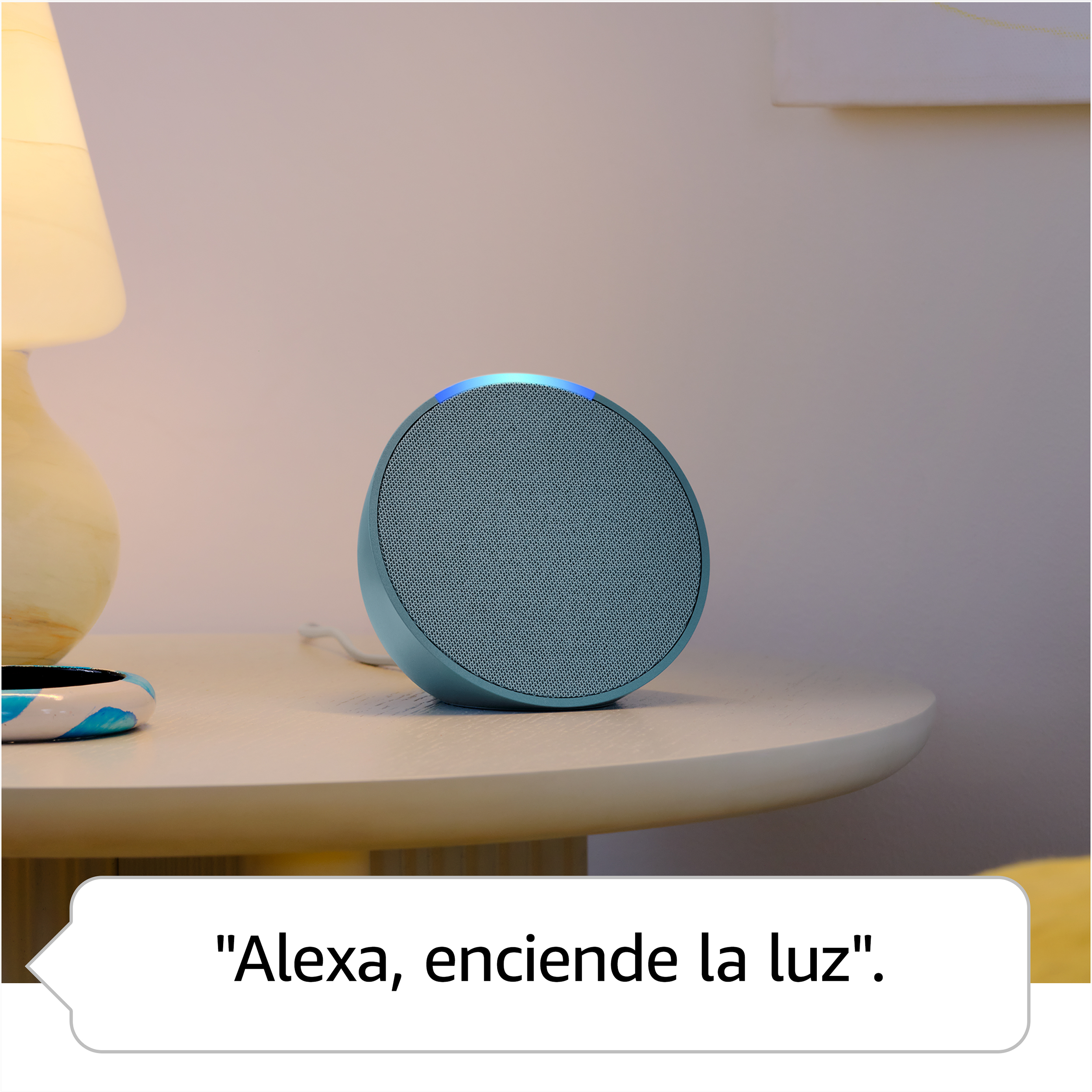Altavoz inteligente azul en una mesa con una burbuja de diálogo, diciendo "Alexa, enciende la luz".