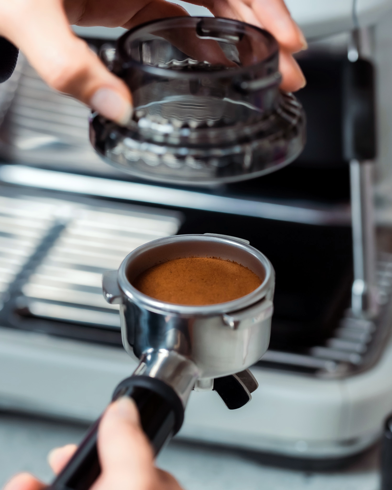 Eine Hand hält einen mit Kaffeepulver gefüllten Siebträger, in der Nähe einer Kaffeemaschine.