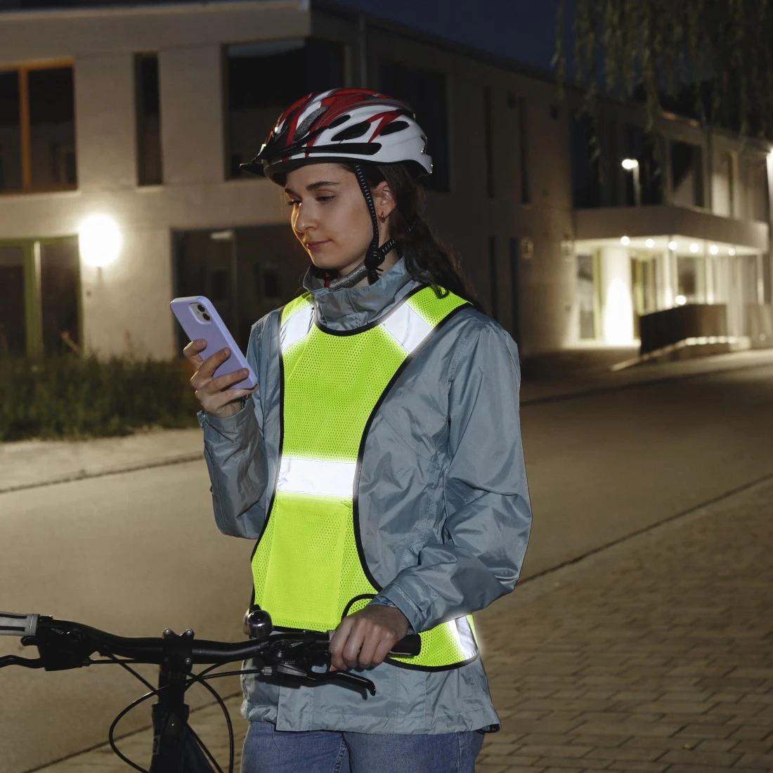Femme avec gilet de sécurité utilise téléphone près d'un vélo la nuit, lumières.