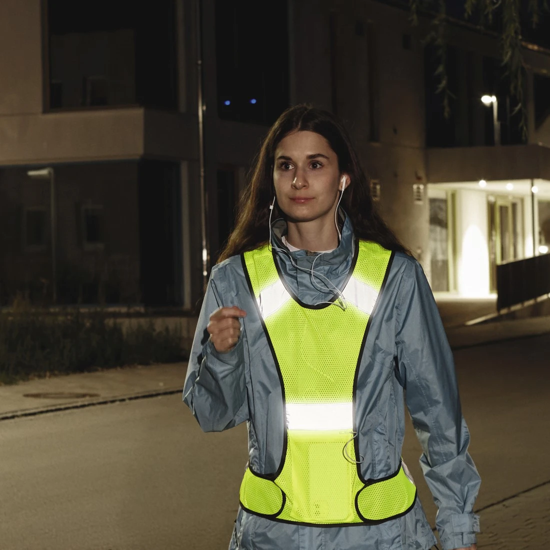 Femme courant la nuit avec un gilet jaune réfléchissant, écoutant de la musique.