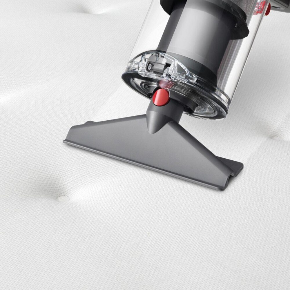 Głowica odkurzacza czyści biały materac z pikowanym wzorem.